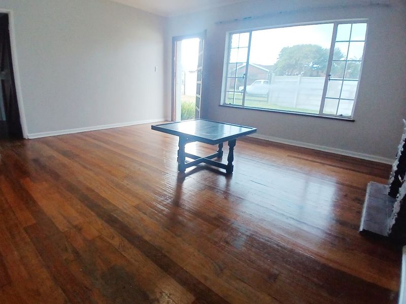 Spacious living room featuring polished hardwood flooring, a large window providing natural light, and a fireplace hearth.