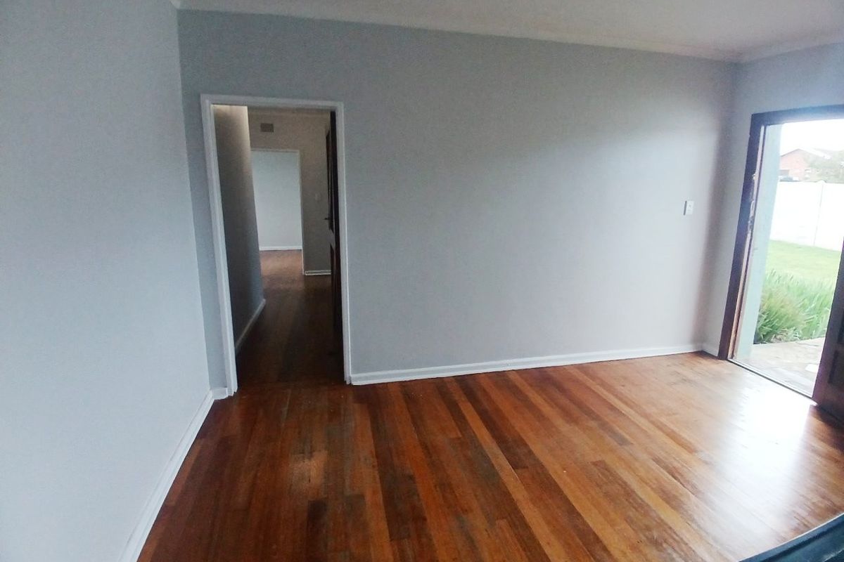 An empty living room featuring polished hardwood flooring, neutral walls, and direct access to an outdoor patio area.