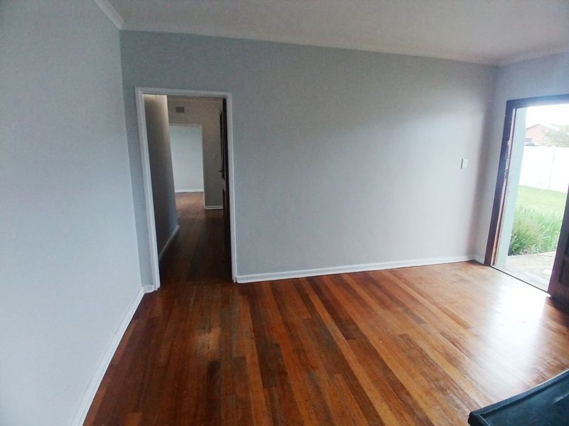 An empty living room featuring polished hardwood flooring, neutral walls, and direct access to an outdoor patio area.