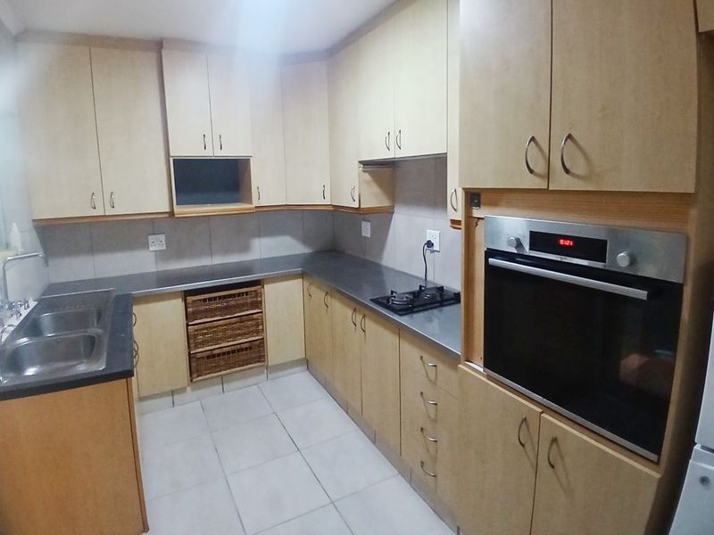 Functional kitchen featuring light wood cabinetry, laminate countertops, built-in oven, gas hob, and tiled flooring with a practical layout.
