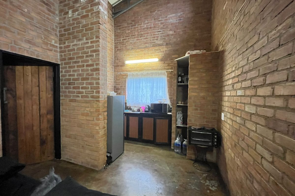 A rustic kitchen area featuring exposed brick walls, vaulted ceilings, concrete flooring, and built-in cabinetry.