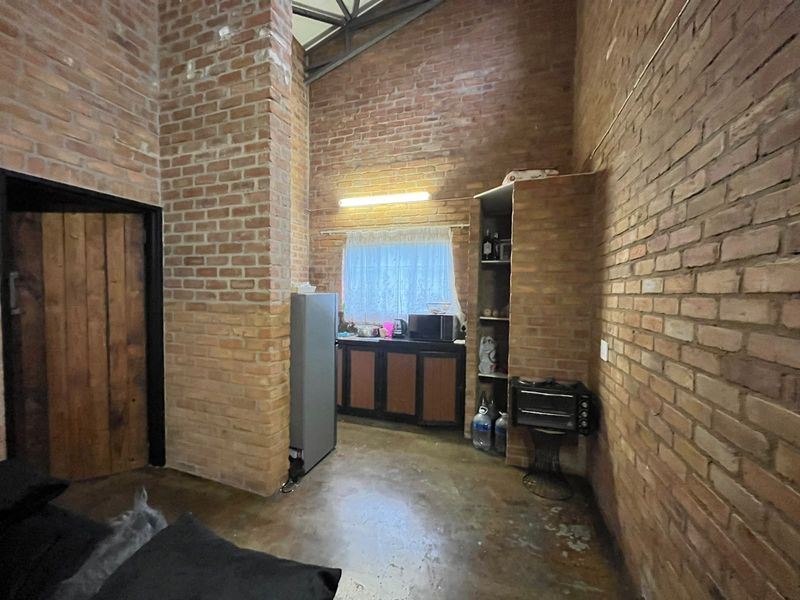 A rustic kitchen area featuring exposed brick walls, vaulted ceilings, concrete flooring, and built-in cabinetry.