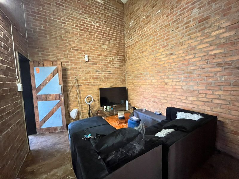 Living room featuring industrial-style exposed brick walls, high ceilings, and concrete flooring, offering a unique character-filled space.