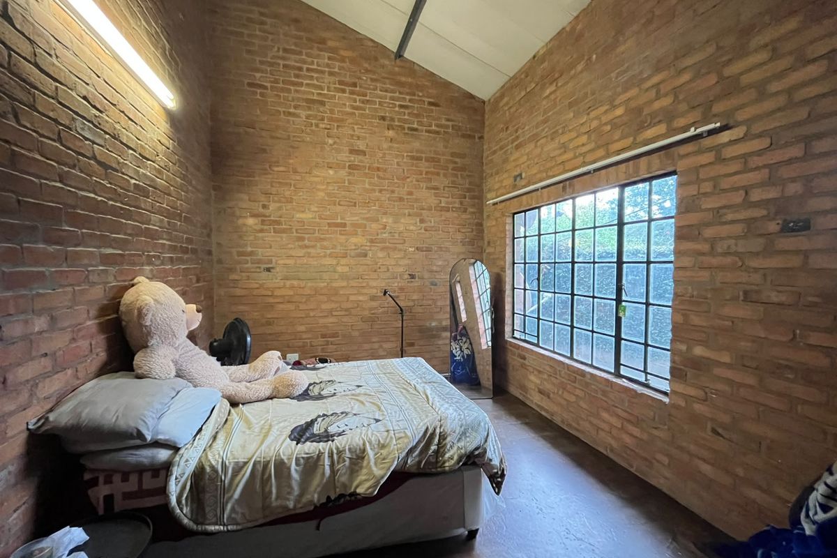 A bedroom featuring exposed brick walls, a high vaulted ceiling, and a large steel-framed window providing natural light.