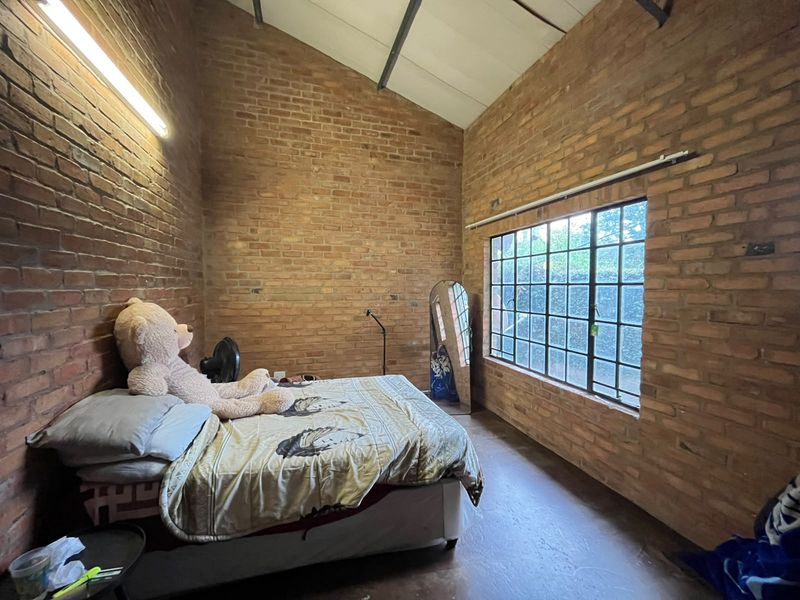 A bedroom featuring exposed brick walls, a high vaulted ceiling, and a large steel-framed window providing natural light.