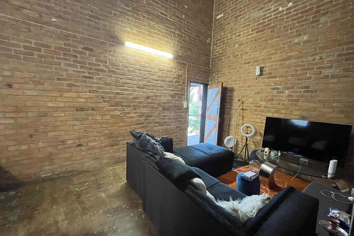 Living room featuring industrial-style exposed brick walls, high ceilings, and polished concrete flooring with direct access to an outdoor area.