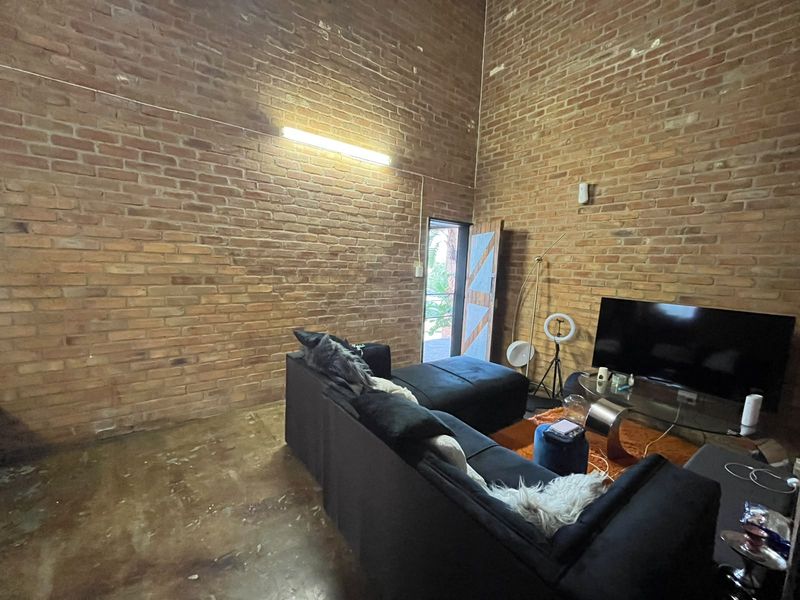 Living room featuring industrial-style exposed brick walls, high ceilings, and polished concrete flooring with direct access to an outdoor area.