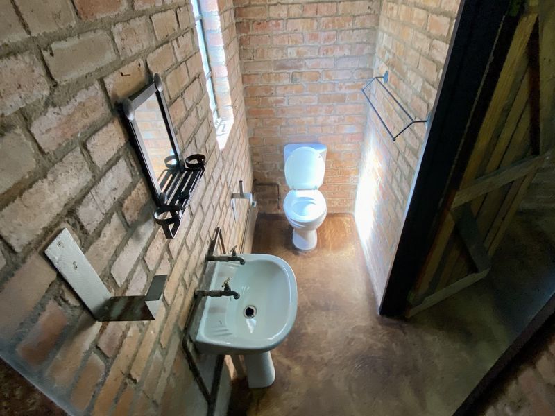 A compact bathroom featuring exposed brick walls, a pedestal basin, and a toilet, offering a rustic industrial aesthetic with potential for modern refinement.