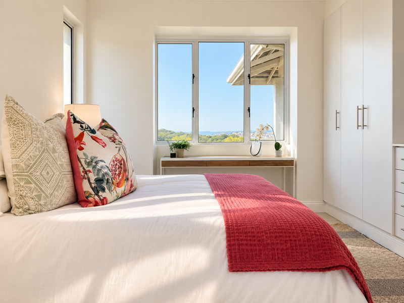 Bright and modern bedroom featuring built-in cupboards, clean finishes, and large windows offering scenic outdoor views.