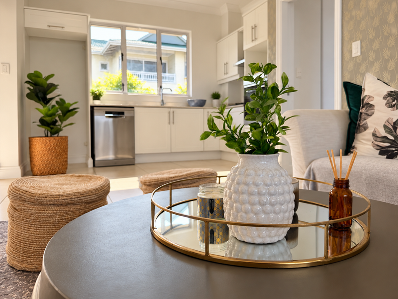 A bright open-plan living and kitchen area featuring modern white cabinetry, stainless steel dishwasher, and neutral tiled flooring.