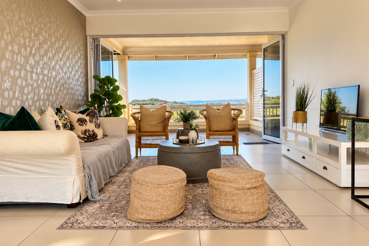 Bright living room featuring large bi-fold doors that open onto a covered patio with scenic views, complemented by neutral tiled flooring and textured wallpaper.