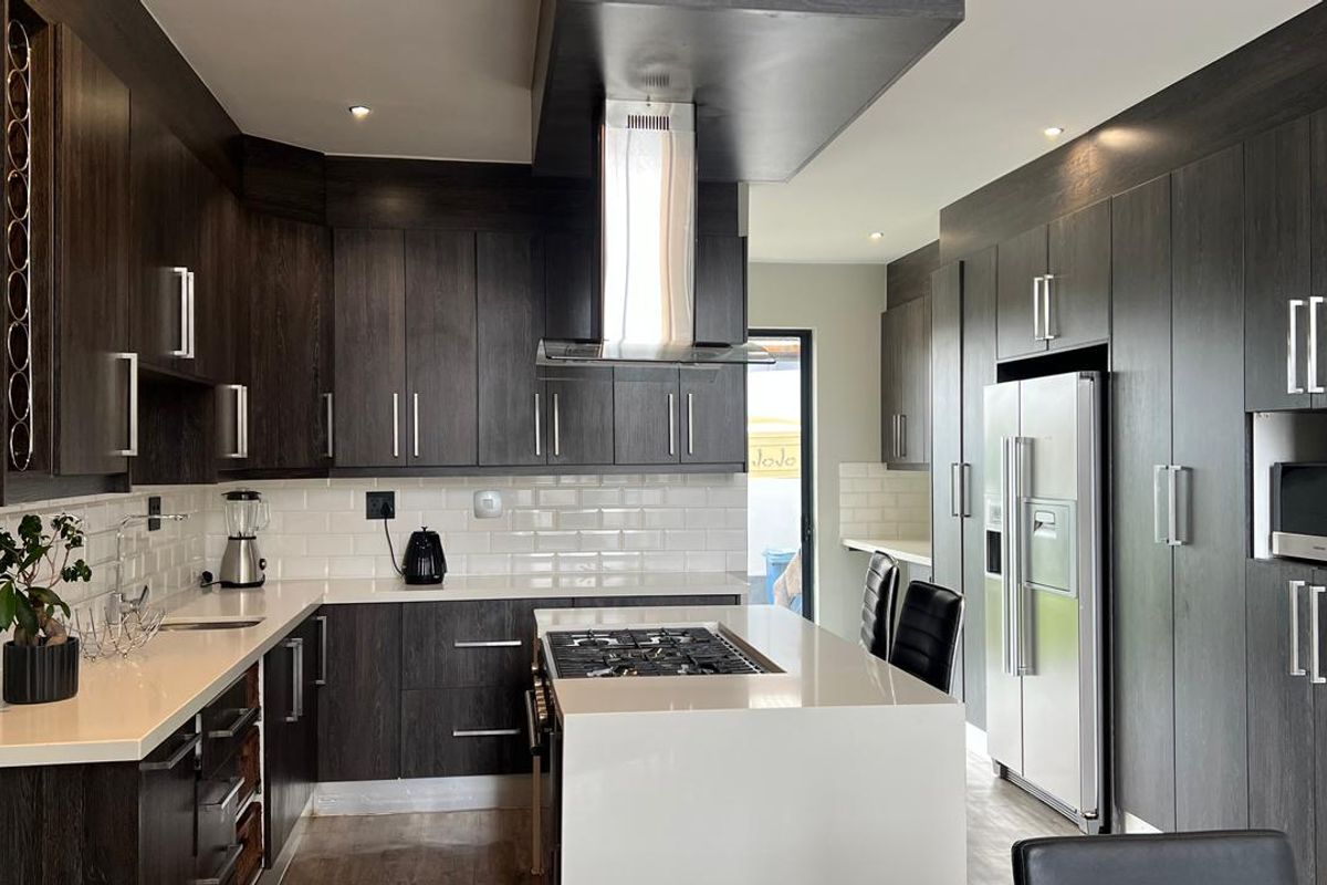 Modern kitchen featuring dark wood cabinetry, white quartz countertops, subway tile backsplash, and integrated stainless steel appliances.