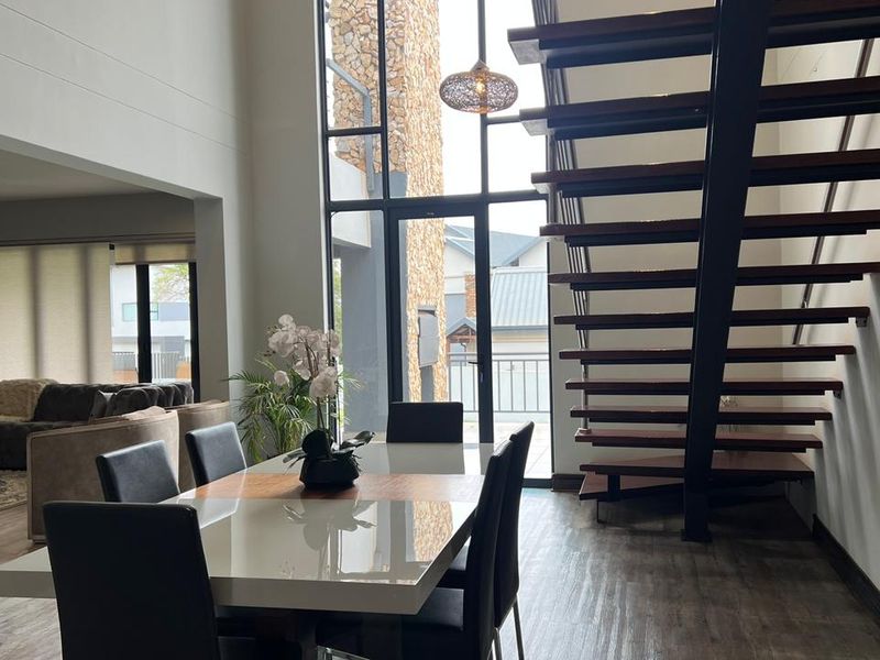 Spacious open-plan dining area featuring a striking floating staircase, double-volume windows, and modern laminate flooring with seamless access to the outdoor space.