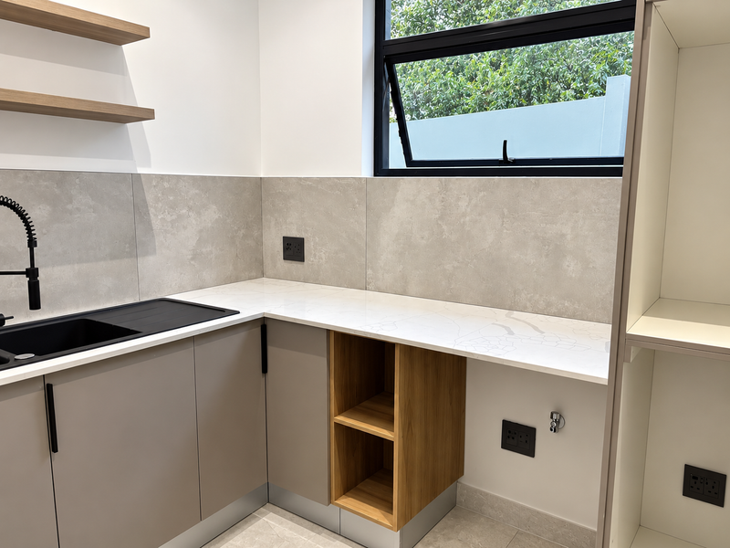 A modern, clean scullery featuring stone countertops, built-in cabinetry, floating shelves, and a sleek black sink with a gooseneck faucet.
