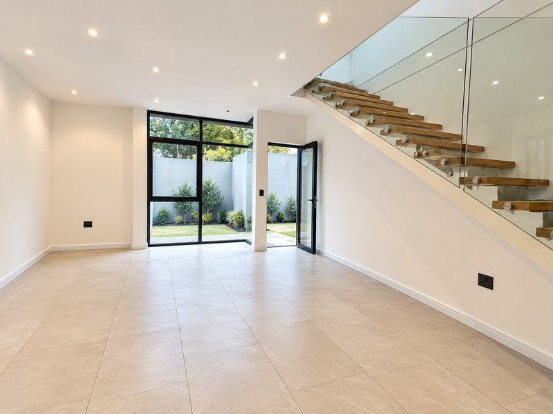Spacious, modern open-plan living area featuring large format floor tiles, a contemporary floating staircase with glass balustrade, and direct access to a private garden.
