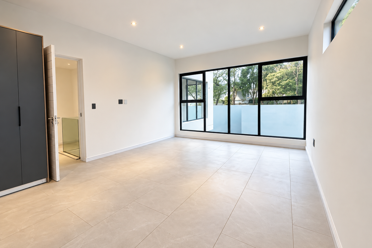 A bright, modern, and spacious bedroom featuring large windows, neutral tiled flooring, and built-in cupboards.