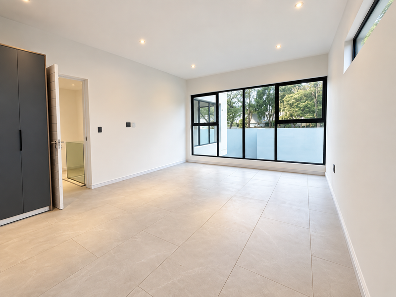 A bright, modern, and spacious bedroom featuring large windows, neutral tiled flooring, and built-in cupboards.