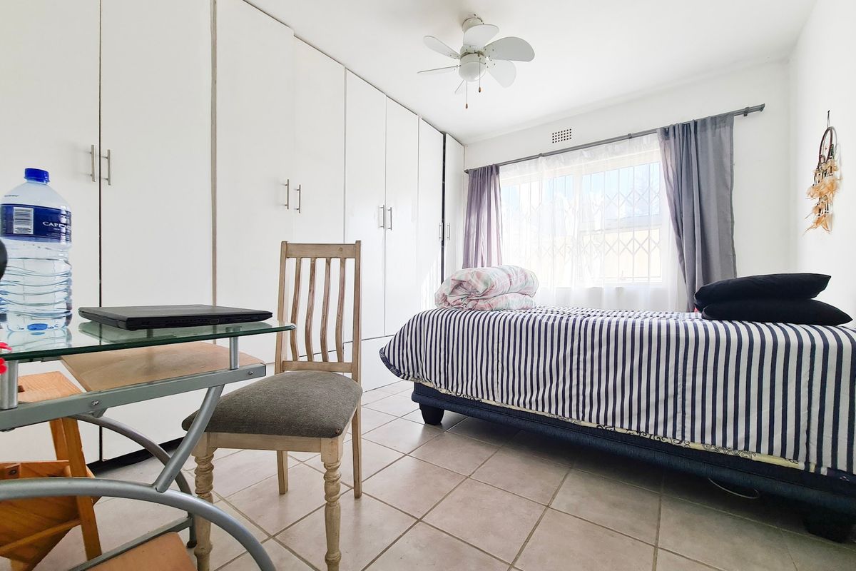 A functional bedroom featuring extensive built-in cupboards, tiled flooring, and a ceiling fan, providing ample storage and comfortable living space.