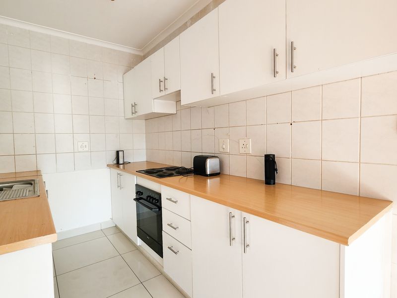 A functional kitchen featuring white cabinetry, laminate countertops, a built-in oven, electric hob, and tiled backsplash with neutral floor tiles.