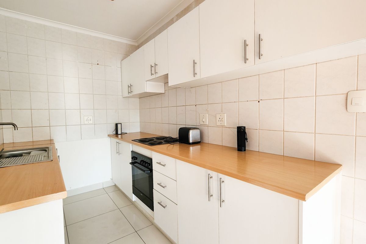 A functional kitchen featuring white cabinetry, laminate countertops, a built-in oven, electric hob, and tiled backsplash with neutral floor tiles.