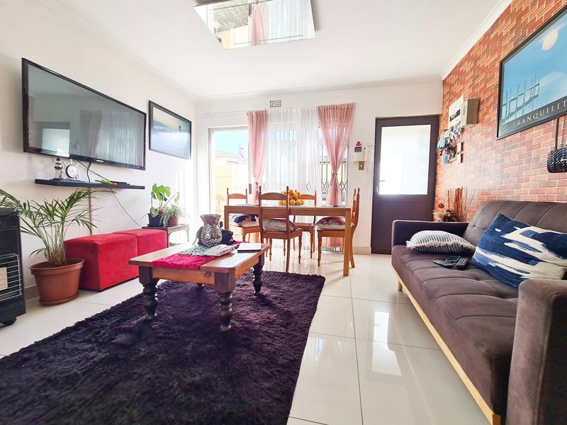 Open-plan living and dining area featuring tiled flooring, a brick-effect feature wall, and direct access to an outdoor space through a sliding glass door.