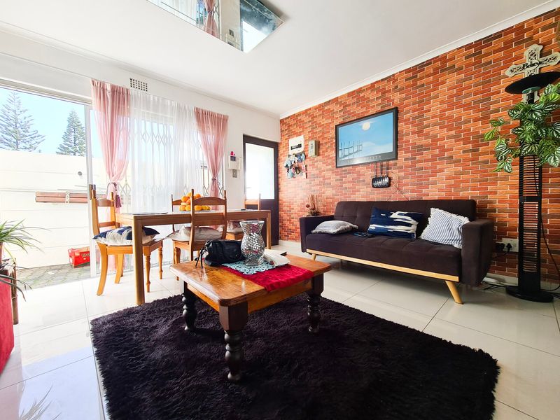 Open-plan living and dining area featuring an exposed brick accent wall, tiled flooring, and large sliding glass doors providing access to the outdoor space.