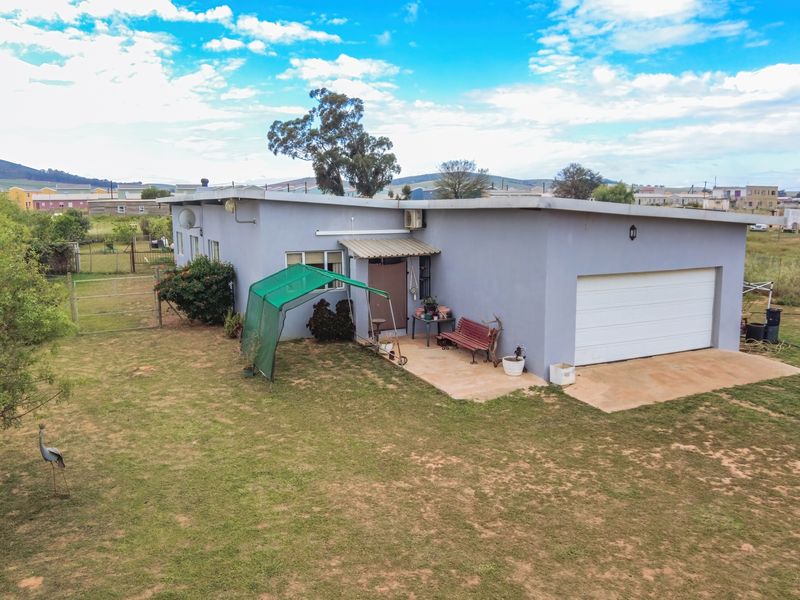 Rear view of the property featuring a single garage, concrete patio area, and surrounding garden space with perimeter fencing.