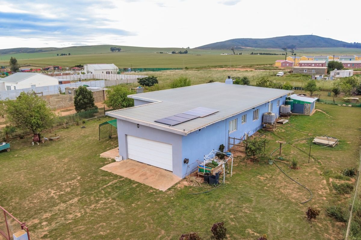 Aerial view of a detached house featuring a metal roof with solar panels, a garage, and surrounding garden space in a rural setting.