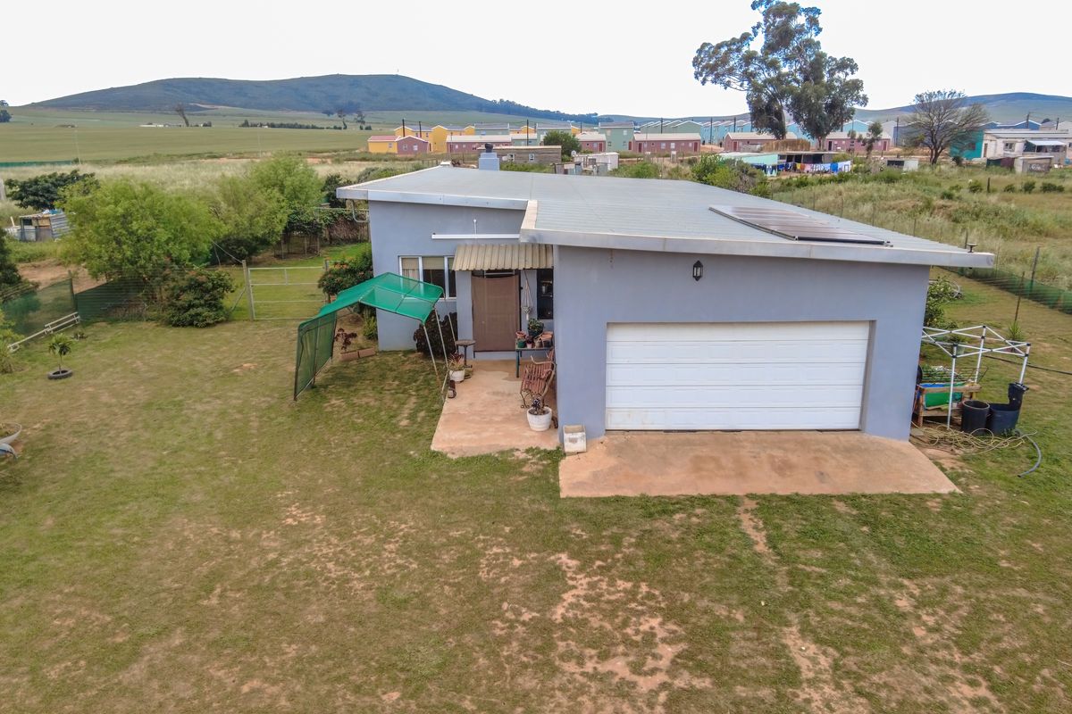 Aerial view of the rear exterior of the house, featuring a single garage, metal roof with solar panels, and a surrounding garden area.