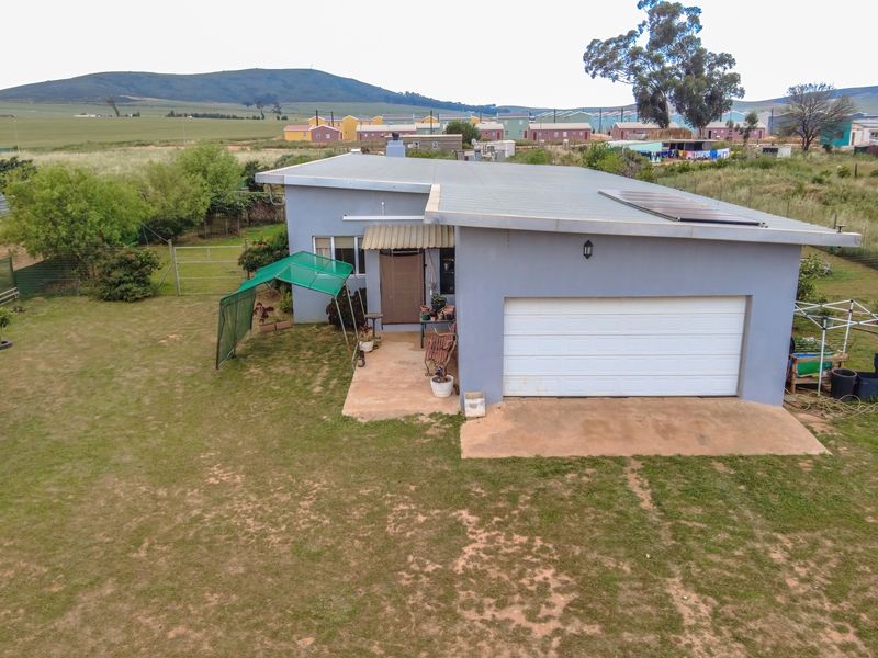 Aerial view of the rear exterior of the house, featuring a single garage, metal roof with solar panels, and a surrounding garden area.