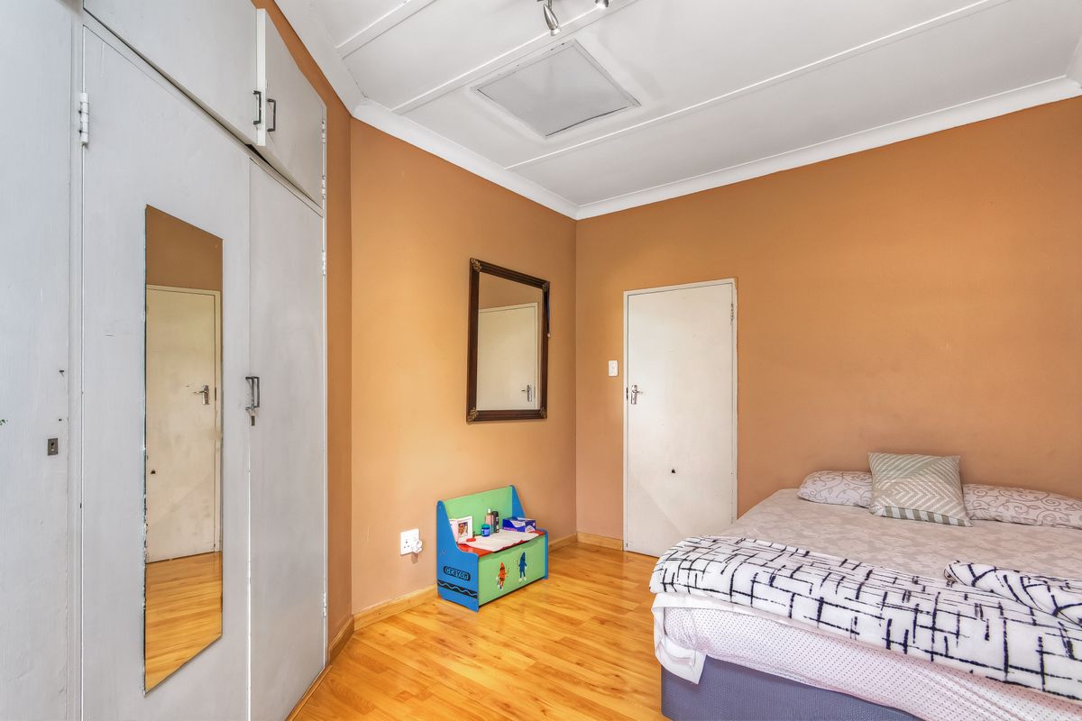 A functional bedroom featuring laminate flooring, built-in wardrobe storage, and neutral wall finishes, offering a practical space for rest.