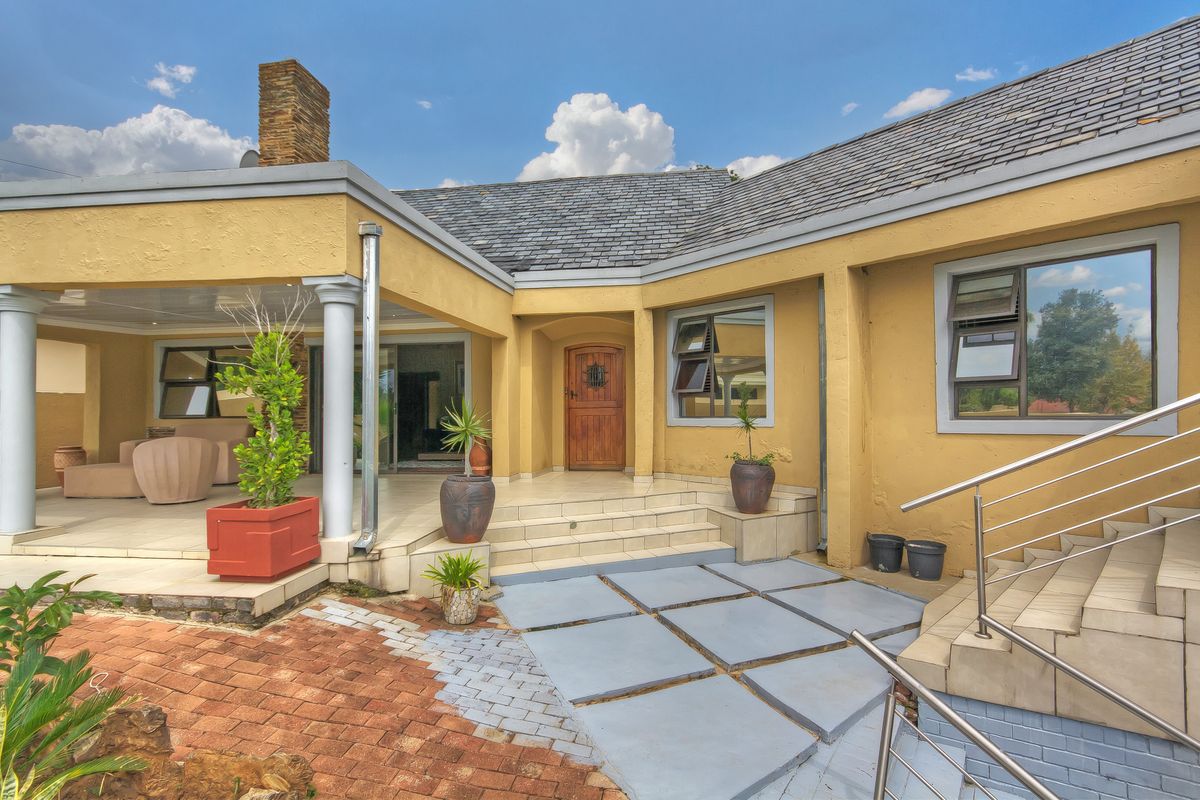 Rear exterior view featuring a covered patio, tiled entrance steps, stone paving, and a prominent brick chimney with a slate roof.