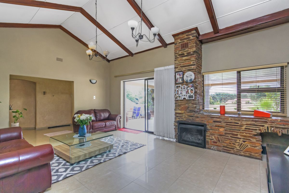Spacious living room featuring a vaulted ceiling with exposed timber beams, a prominent stone fireplace, tiled flooring, and direct access to the patio.
