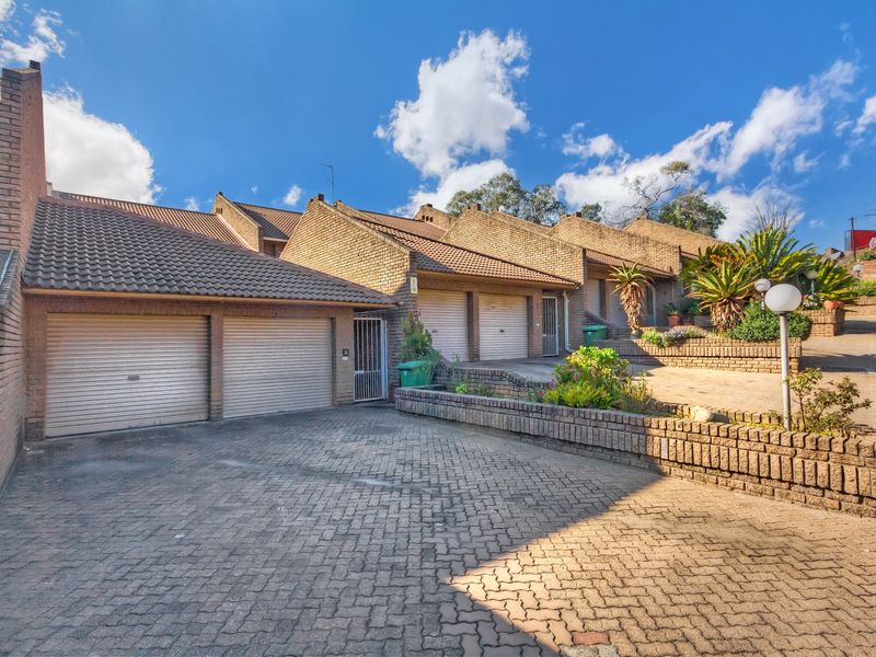 Front exterior view of a townhouse complex featuring brick facade, multiple roller garage doors, and a paved driveway with tiered brick retaining walls.