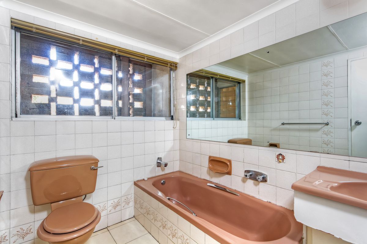 A dated bathroom featuring original brown sanitary ware, tiled walls, a large wall mirror, and a unique breeze block window detail.