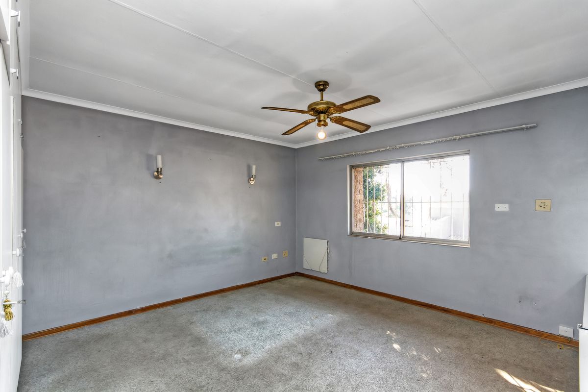 An empty bedroom featuring a ceiling fan, wall sconces, and a window with security bars, offering a blank canvas for renovation.