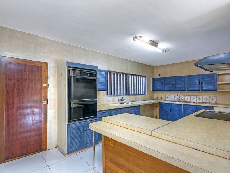 A spacious, dated kitchen featuring blue cabinetry, built-in oven, hob, extractor fan, and tiled finishes, offering significant potential for a modern renovation.