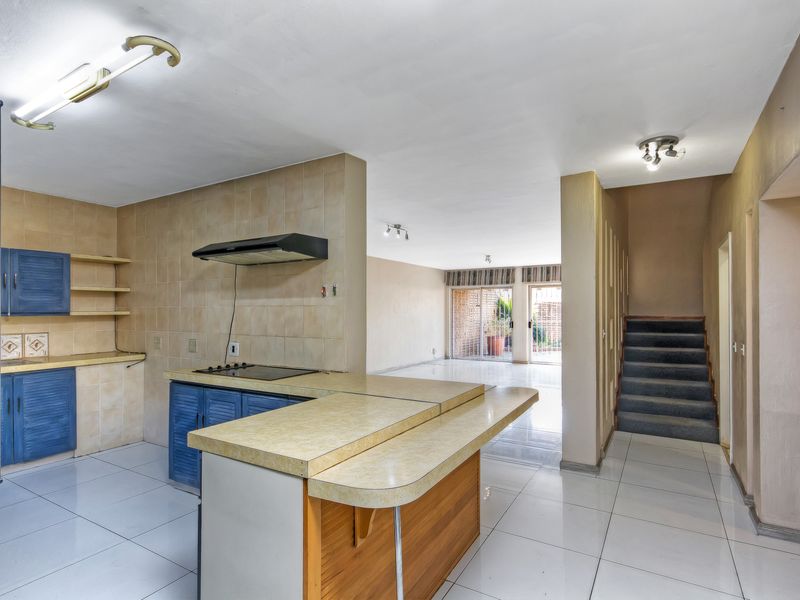 Open-plan kitchen and living area featuring tiled floors, built-in cabinetry, and a staircase leading to the upper level with access to the rear patio.