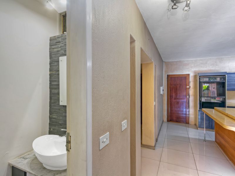 Open plan area featuring a guest bathroom with stone accent wall, tiled flooring, and a kitchen area with built-in oven and breakfast bar.
