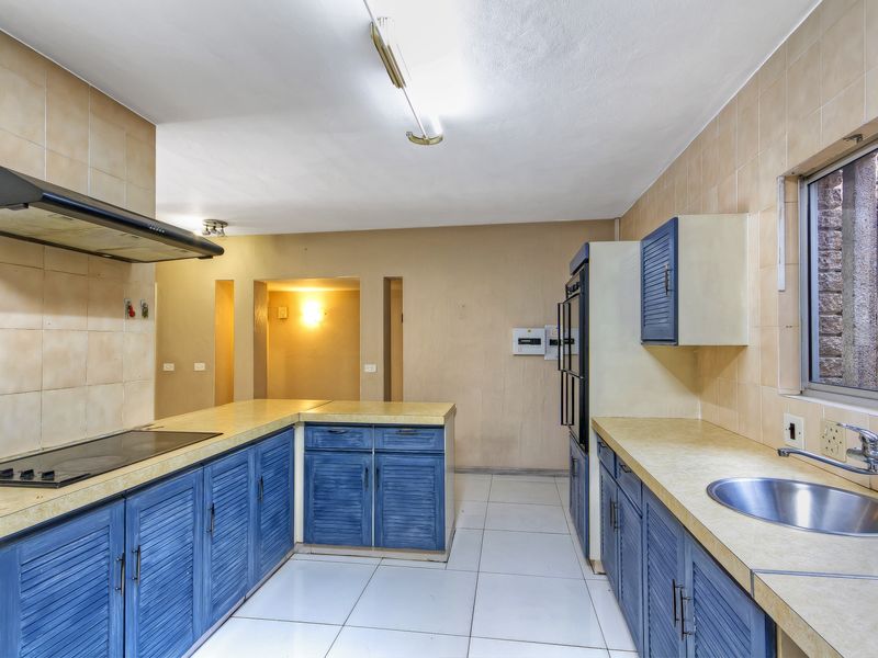 A functional kitchen featuring blue built-in cabinetry, laminate countertops, a stainless steel sink, and integrated cooking appliances with tiled flooring and backsplash.