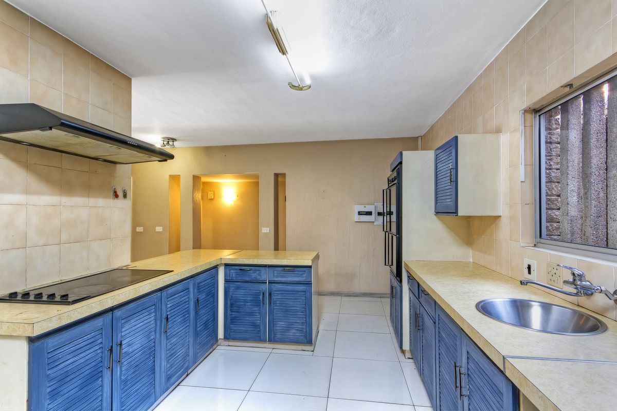 A functional kitchen featuring blue built-in cabinetry, laminate countertops, a stainless steel sink, and integrated cooking appliances with tiled flooring and backsplash.