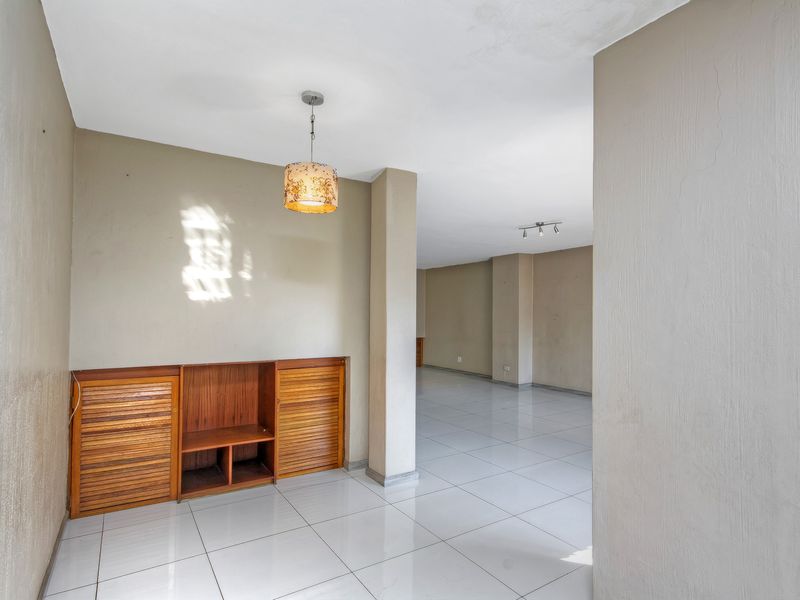 Spacious open-plan living area featuring neutral tiled flooring, built-in wooden cabinetry, and a combination of pendant and recessed ceiling lighting.