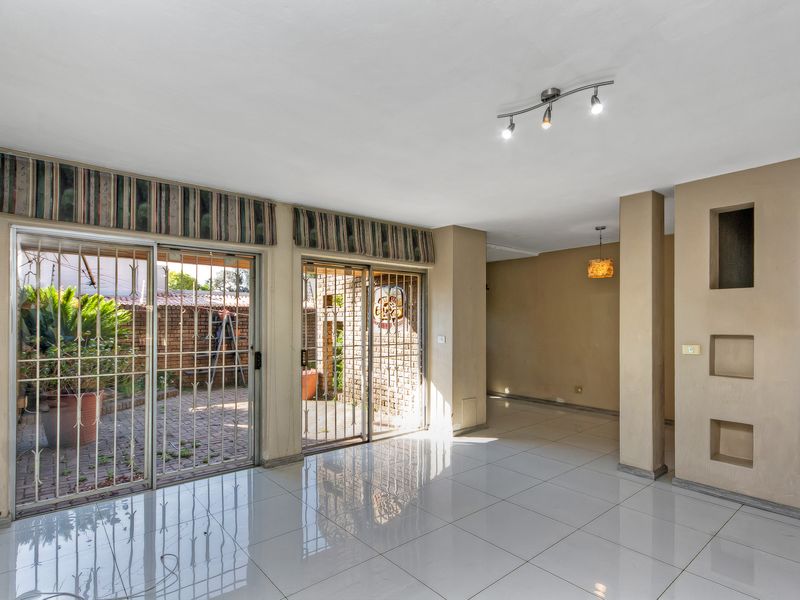 Spacious, empty living area featuring large sliding glass doors with security gates, tiled flooring, and decorative wall niches, opening onto a paved patio.