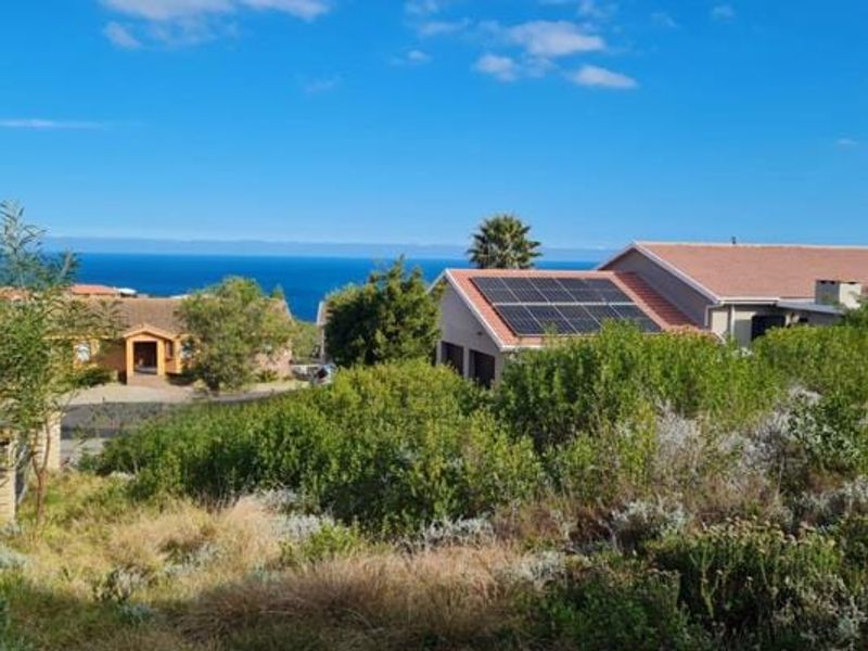 A scenic view overlooking a residential area with coastal ocean vistas and visible solar panel installations on neighboring rooftops.