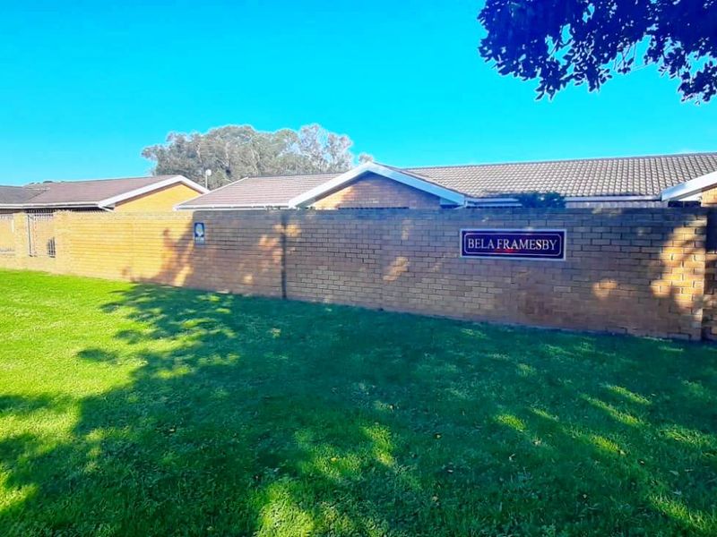 Exterior view of the Bela Framesby townhouse complex featuring a brick boundary wall, tiled roofing, and a well-maintained lawn area.
