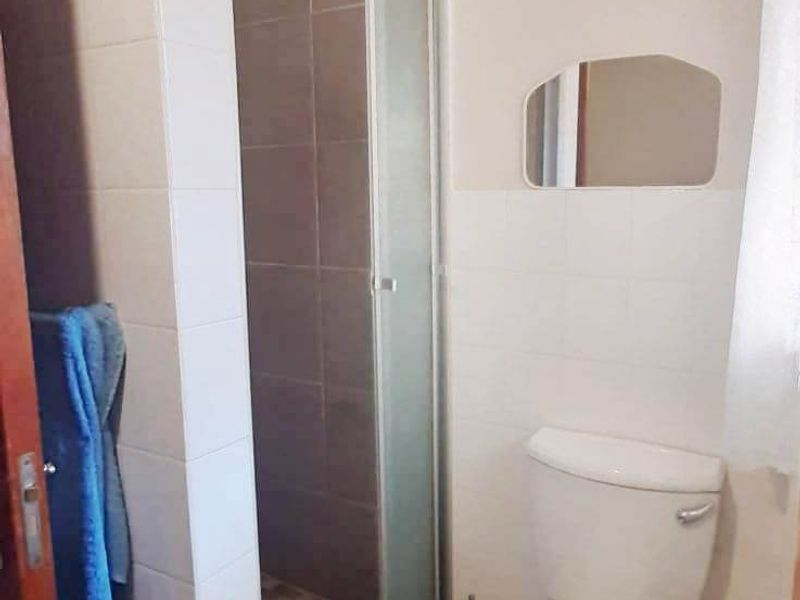 A functional bathroom featuring a tiled shower enclosure and a standard toilet, finished with neutral wall tiles.