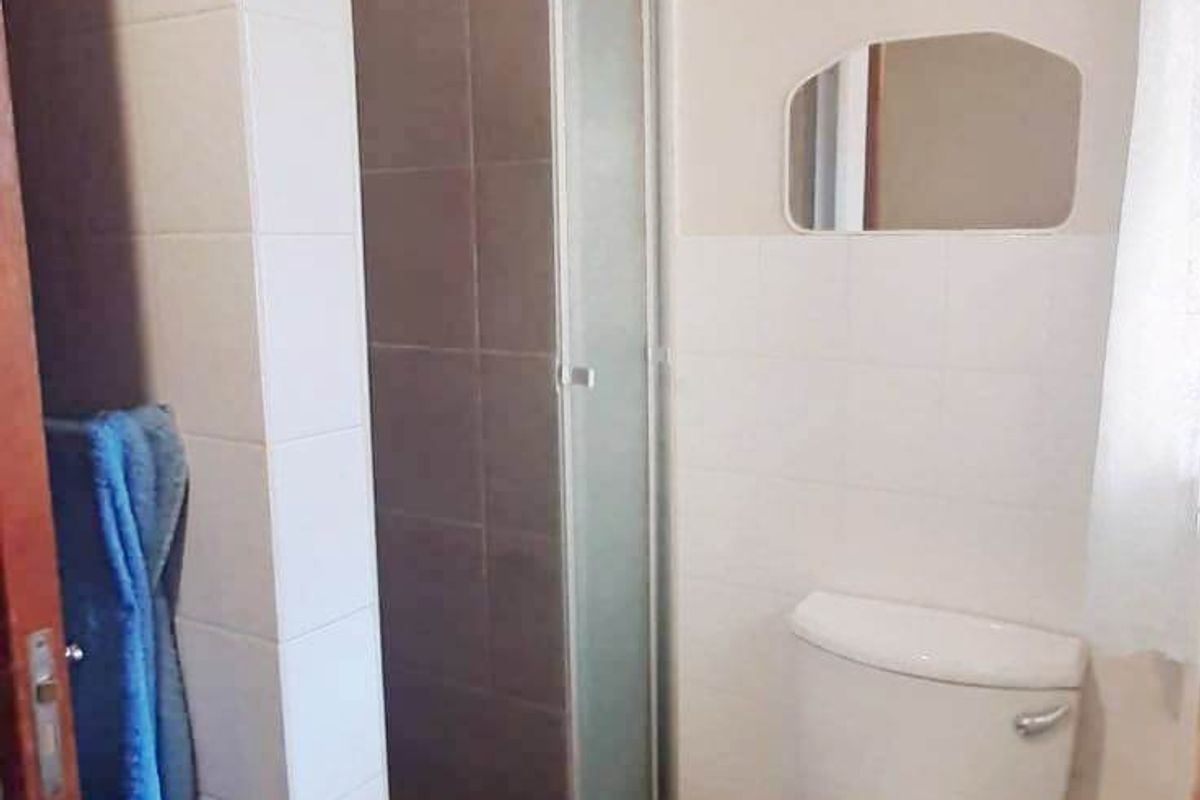 A functional bathroom featuring a tiled shower enclosure and a standard toilet, finished with neutral wall tiles.
