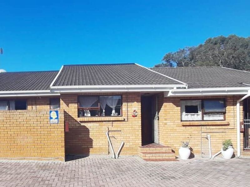 Front elevation of a face brick townhouse featuring a tiled roof, paved driveway, and secure entrance with security gate.