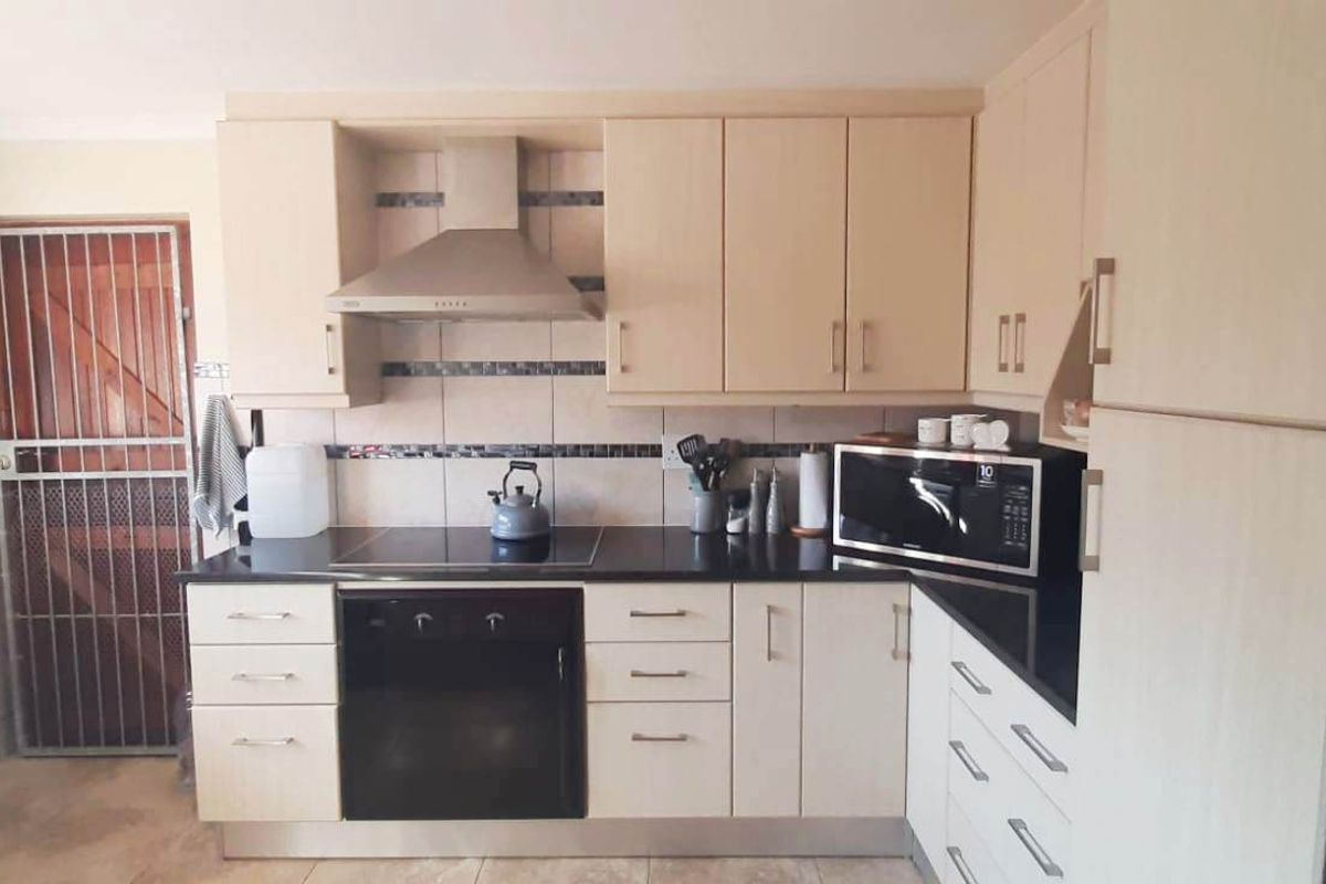 Functional kitchen featuring light-toned cabinetry, granite countertops, built-in oven and hob, extractor fan, and a tiled backsplash with a rear security door.