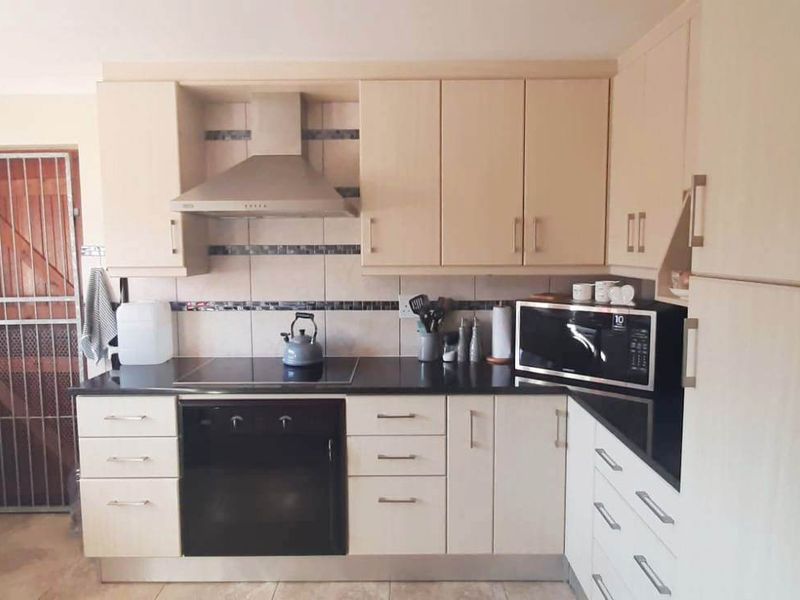 Functional kitchen featuring light-toned cabinetry, granite countertops, built-in oven and hob, extractor fan, and a tiled backsplash with a rear security door.